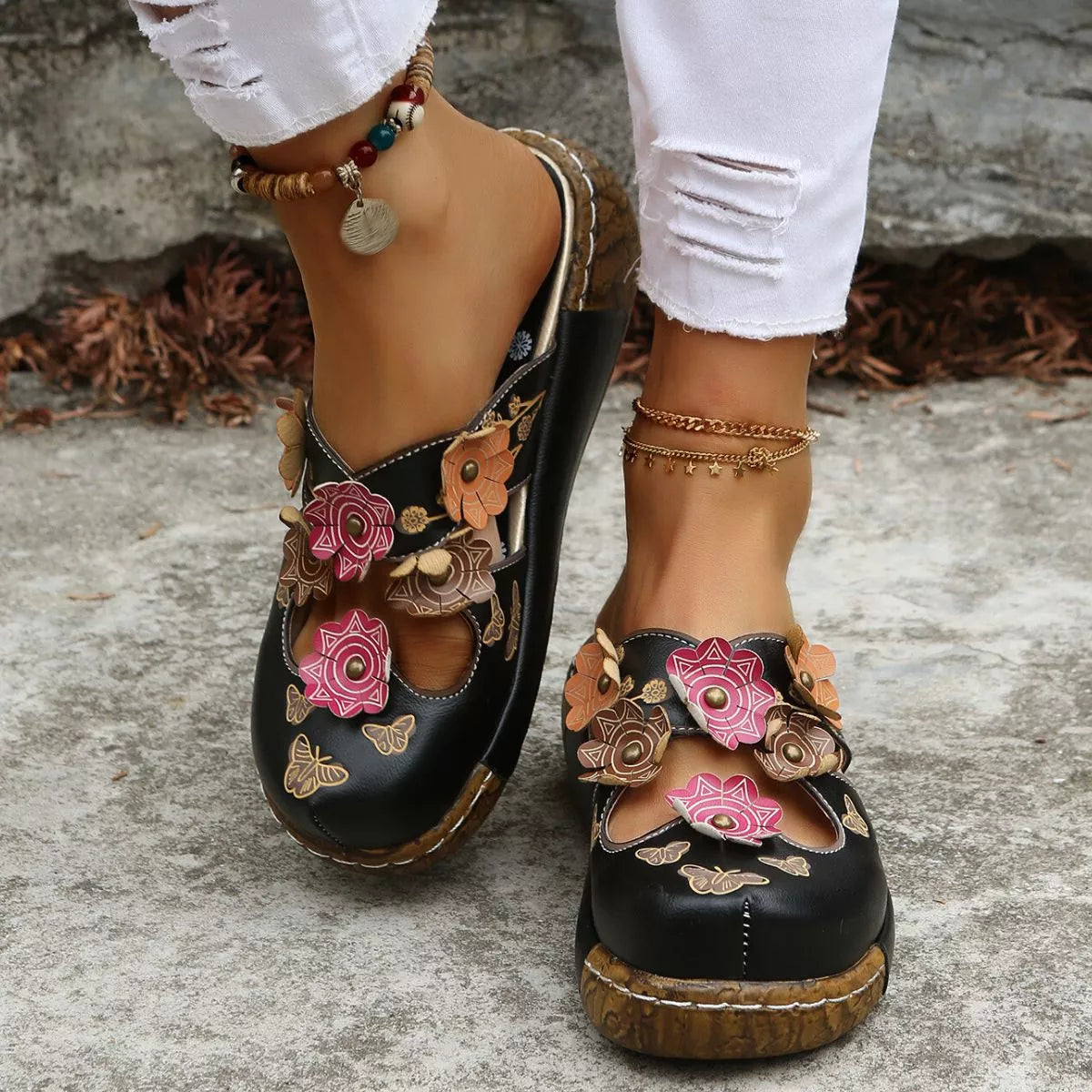 NEWYORKLISTED SHOE COLLECTION: Black floral sandals worn with white pants on a stone surface