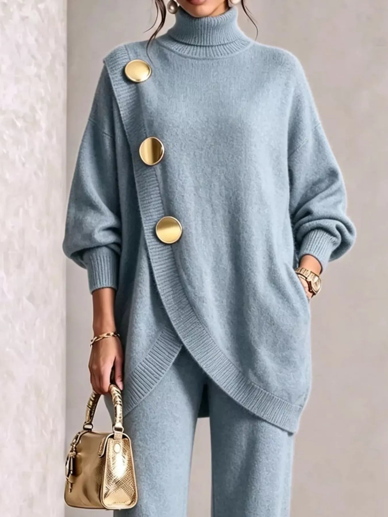 NEWYORKLISTED STYLE COLLECTION:  A woman wearing a light blue knit turtleneck sweater with oversized gold buttons and matching knit pants, holding a small metallic gold handbag against a neutral indoor background.