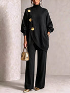 NEWYORKLISTED STYLE COLLECTION:  A model wearing a black knit turtleneck sweater with oversized sleeves and three prominent gold buttons, paired with black wide-leg trousers and holding a small metallic gold handbag.