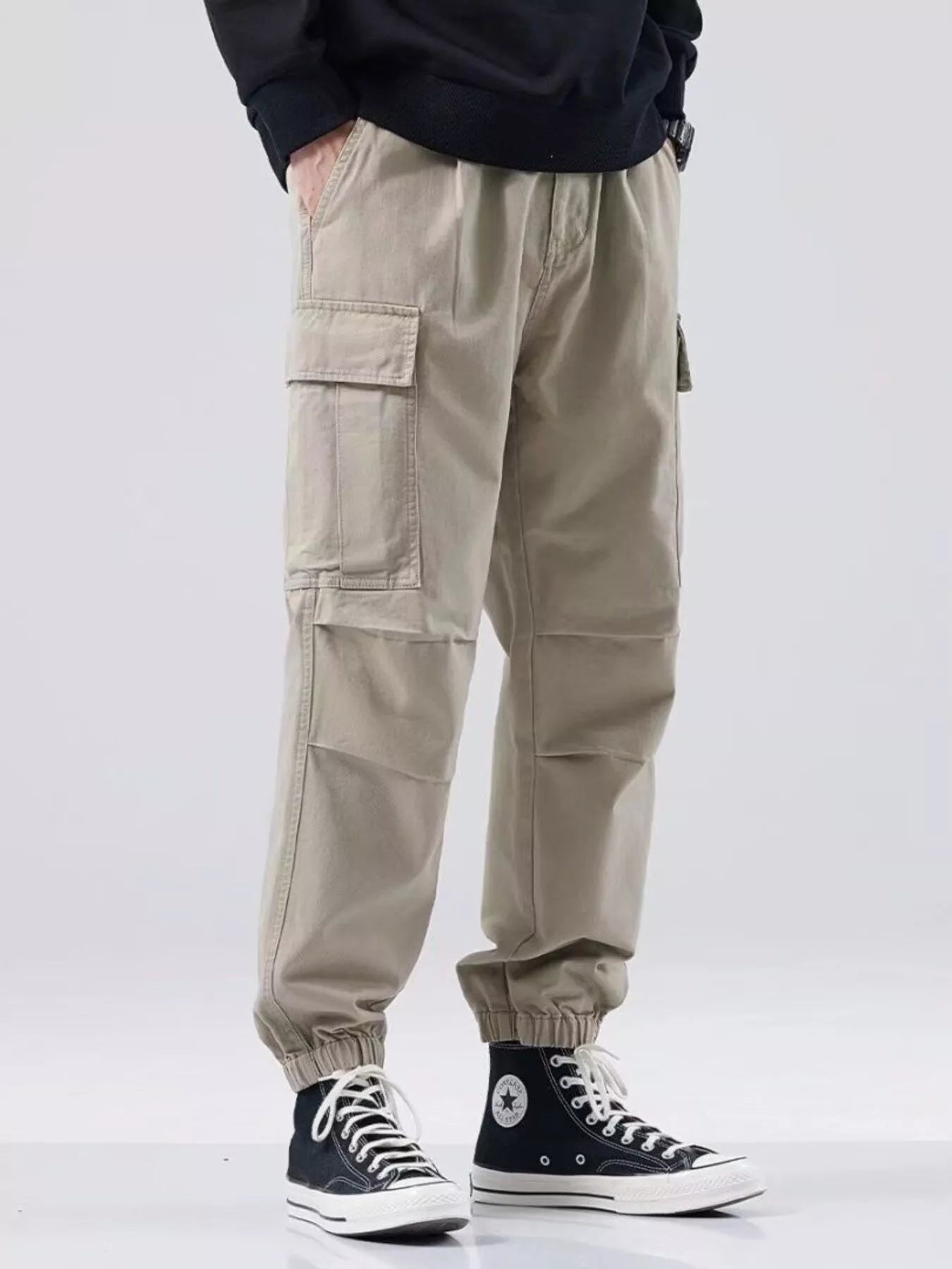 NEWYORKLISTED ATLAS MEN'S COLLECTION: Person wearing beige cargo pants and black high-top sneakers on a white background