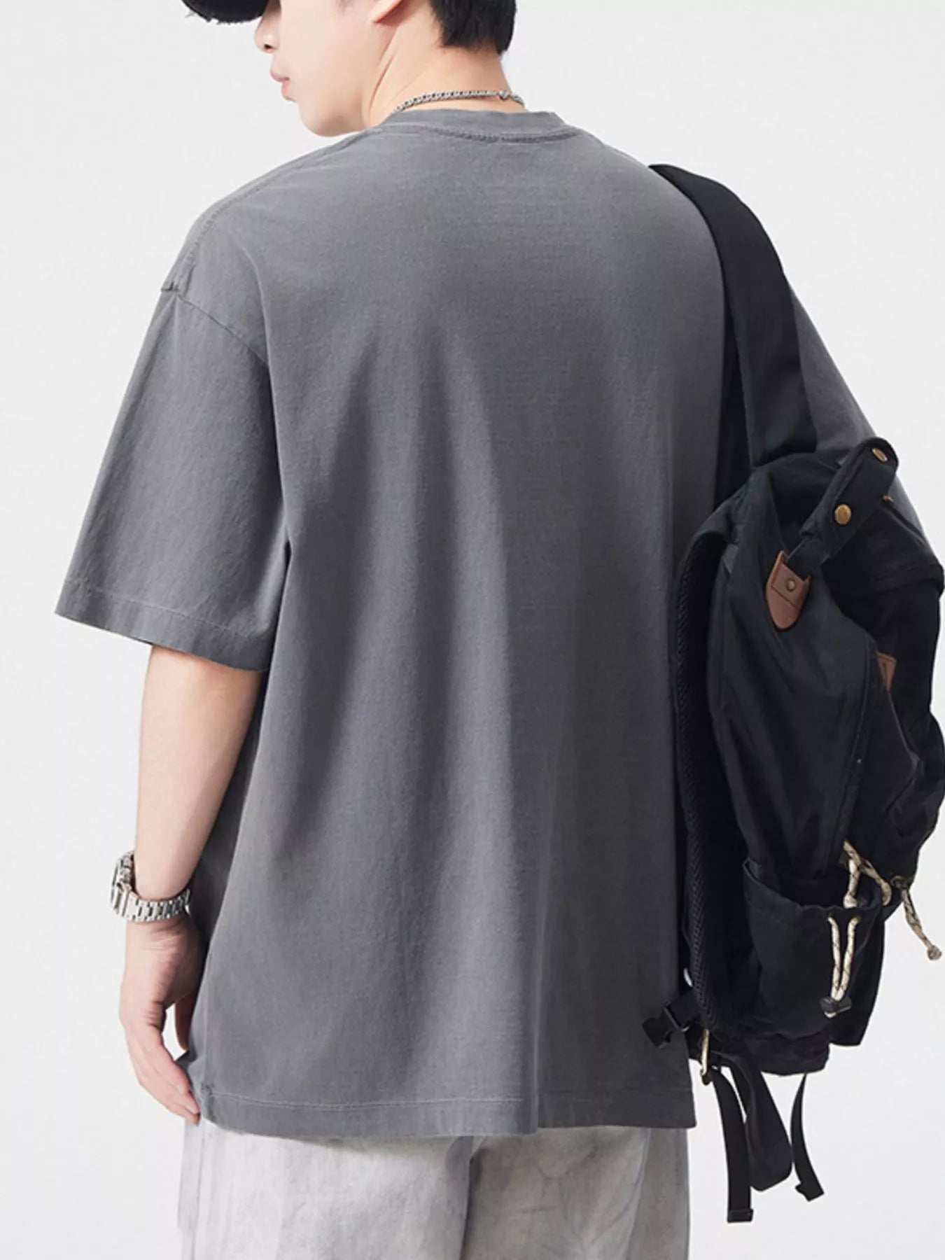 NEWYORKLISTED ATLAS MEN's COLLECTION: Person wearing a gray t-shirt and light-colored pants with a black backpack on a white background
