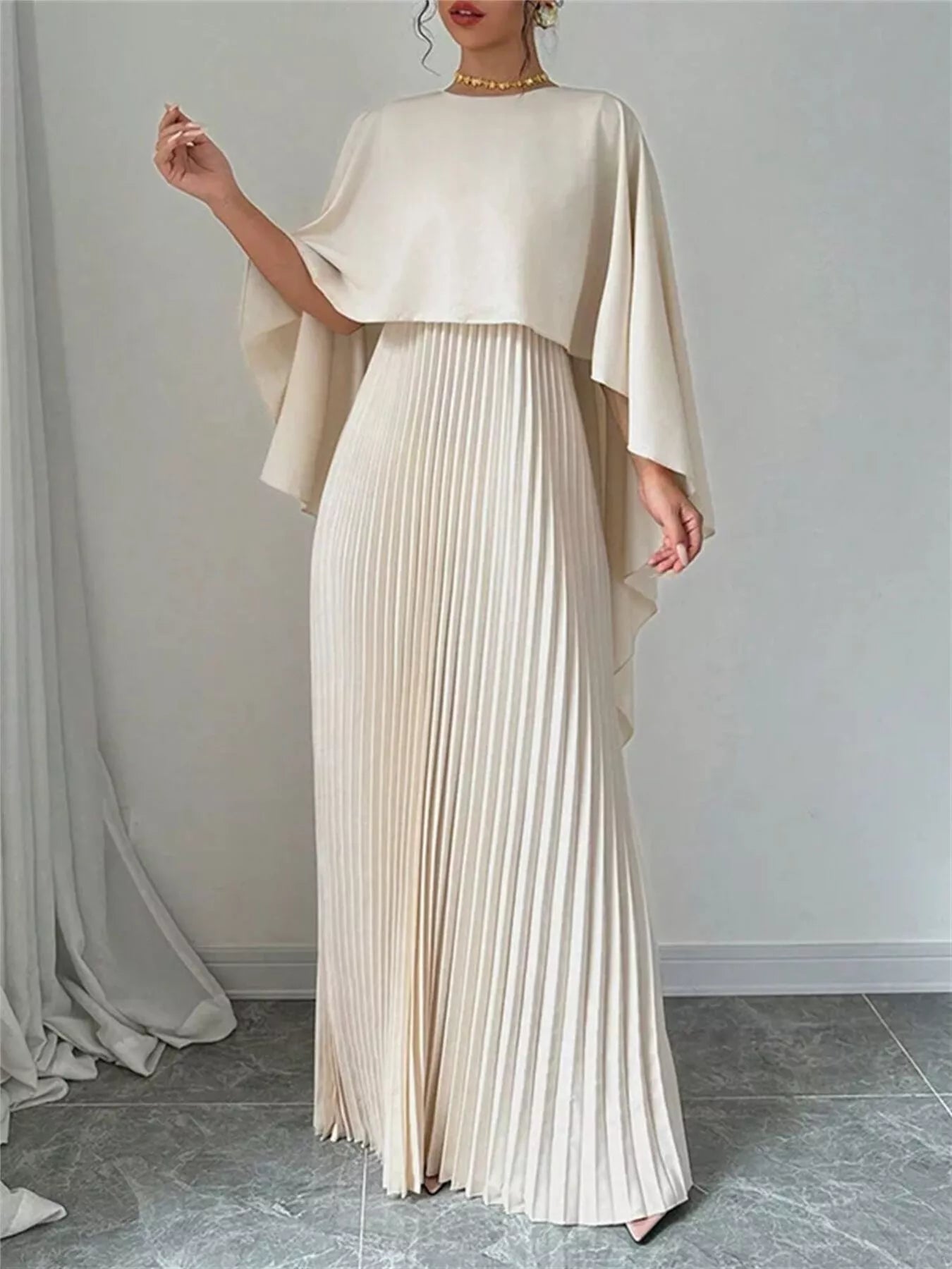 NEWYORKLISTED STYLE COLLECTION: Woman wearing a long, flowing beige dress with a draped top against a plain background