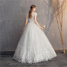 Woman in a white lace wedding dress holding a bouquet against a textured wall.