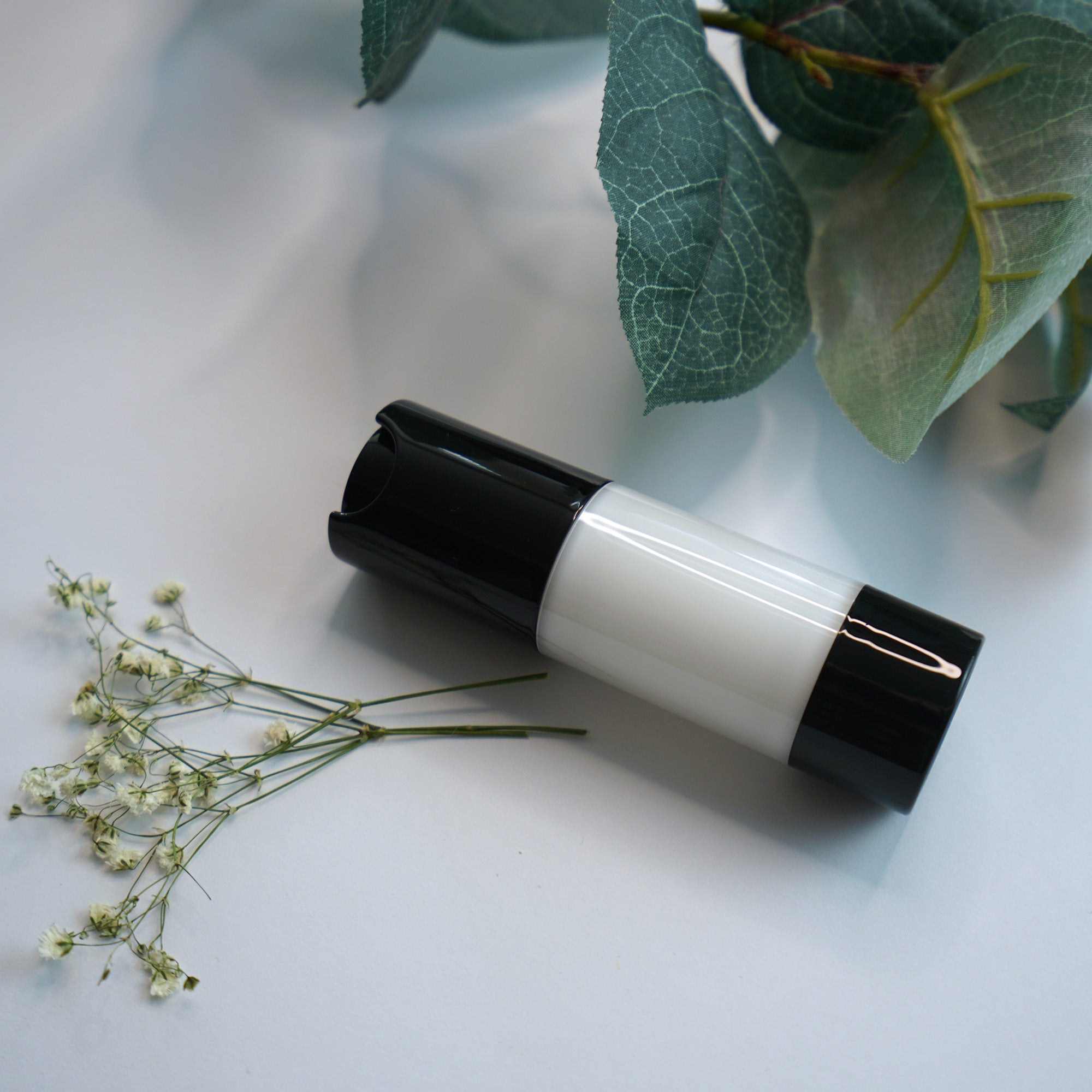 NEWYORKLISTED COSMETIC COLLECTION: Extreme Moisture Blend: bottle with black cap and white body on a light surface with green leaves and flowers.