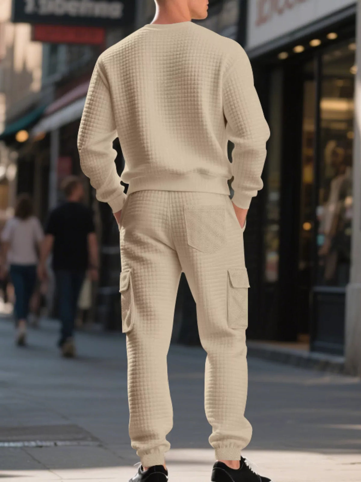 NEWYORKLISTED ATLAS MEN'S COLLECTION: A man viewed from behind wearing a cream-colored waffle-knit crewneck sweatshirt and matching cargo jogger pants on a city sidewalk.