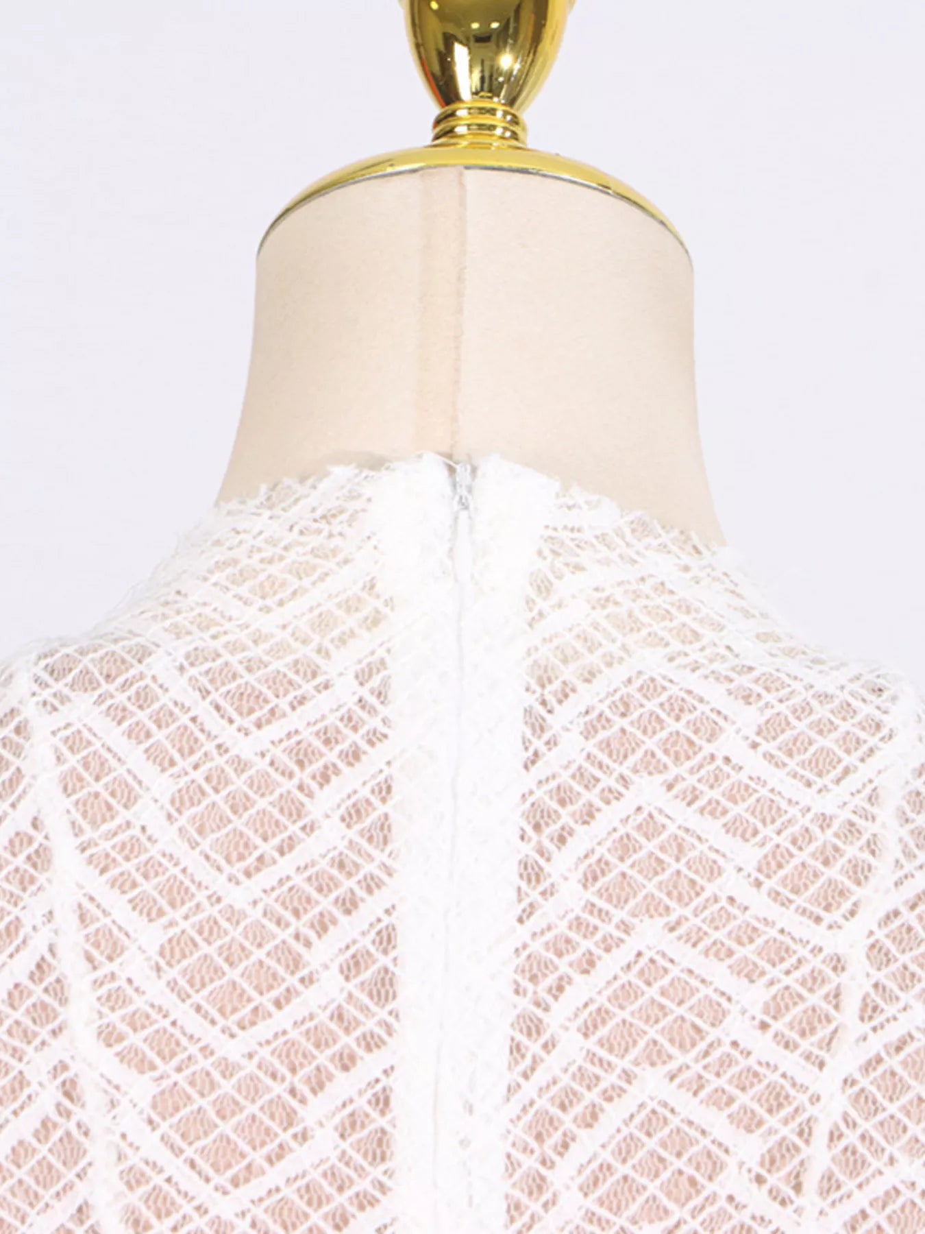 White lace garment on a mannequin with a gold top against a white background