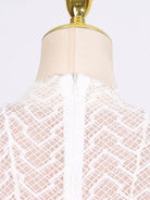White lace garment on a mannequin with a gold top against a white background