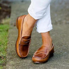 NEWYORKLISTED SHOE COLLECTION: Brown loafers worn with white pants on a blurred outdoor background