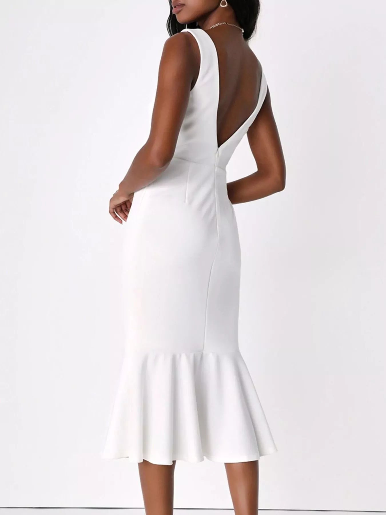 NEWYORKLISTED STYLE COLLECTION: A woman modeling a white sleeveless midi dress from the back, featuring a deep open back, fitted silhouette, and flared ruffled hem, set against a plain white studio background.