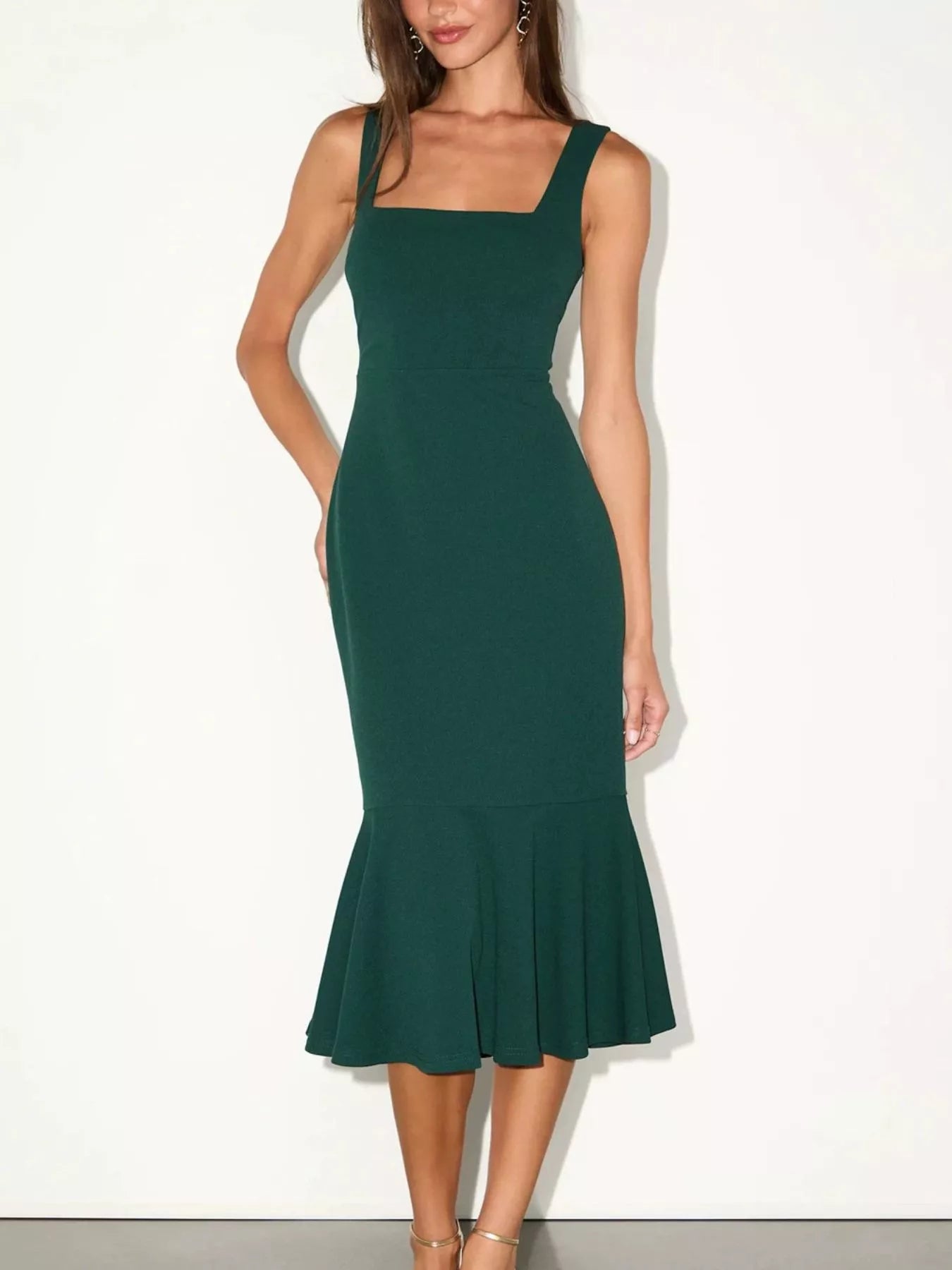 NEWYORKLISTED STYLE COLLECTION: A woman modeling a dark green sleeveless midi dress with a square neckline, fitted silhouette, and flared ruffled hem against a plain white studio background.