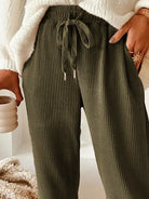 NEWYORKLISTED STYLE COLLECTION: Person wearing olive green ribbed pants with a white sweater and beige background