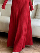 NEWYORKLISTED STYLE COLLECTION: A person wearing a long-sleeve, floor-length red ribbed knit dress standing in front of a light beige sofa on a wood floor.