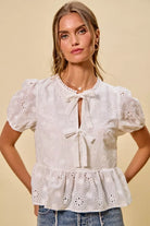 NEWYORKLISTED STYLE COLLECTION:  Woman wearing a white embroidered blouse with puffed sleeves on a beige background