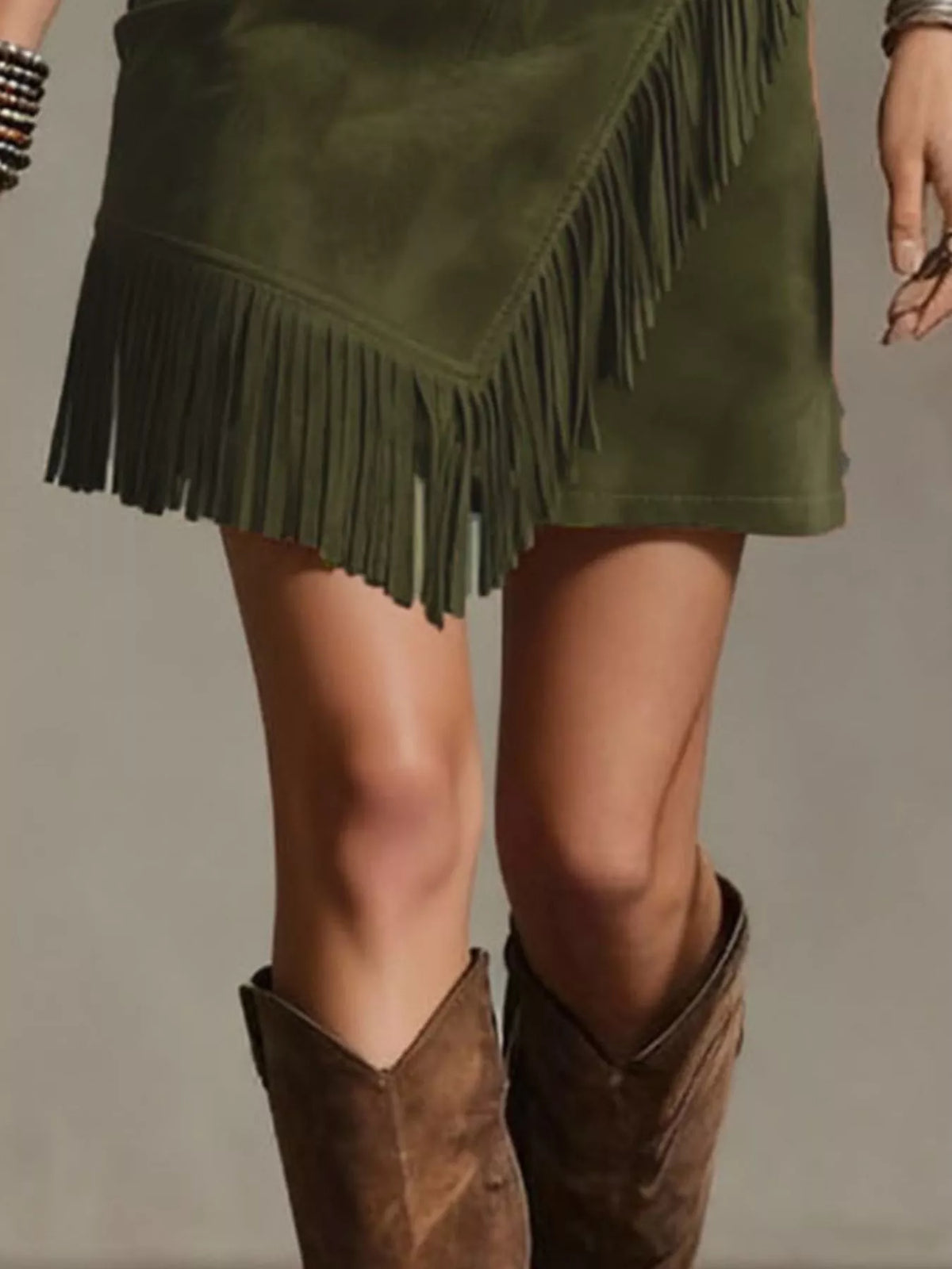 NEWYORKLISTED STYLE COLLECTION: An olive green faux-suede mini skirt with asymmetrical fringe trim, styled with brown suede cowboy boots against a neutral studio background.