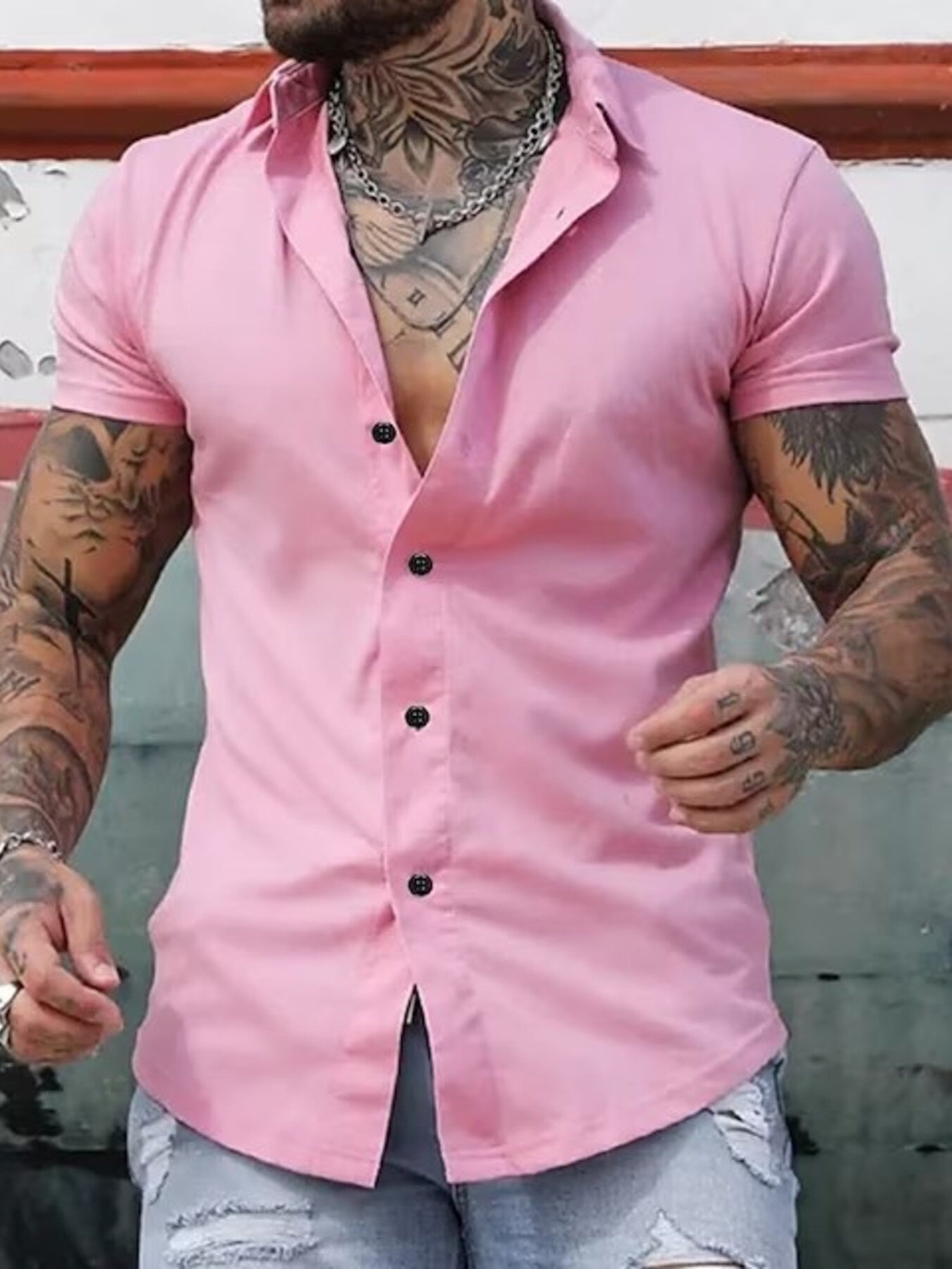 NEWYORKLISTED ATLAS MEN's COLLECTION: Man wearing a pink short-sleeve shirt with black buttons, standing against a neutral background.