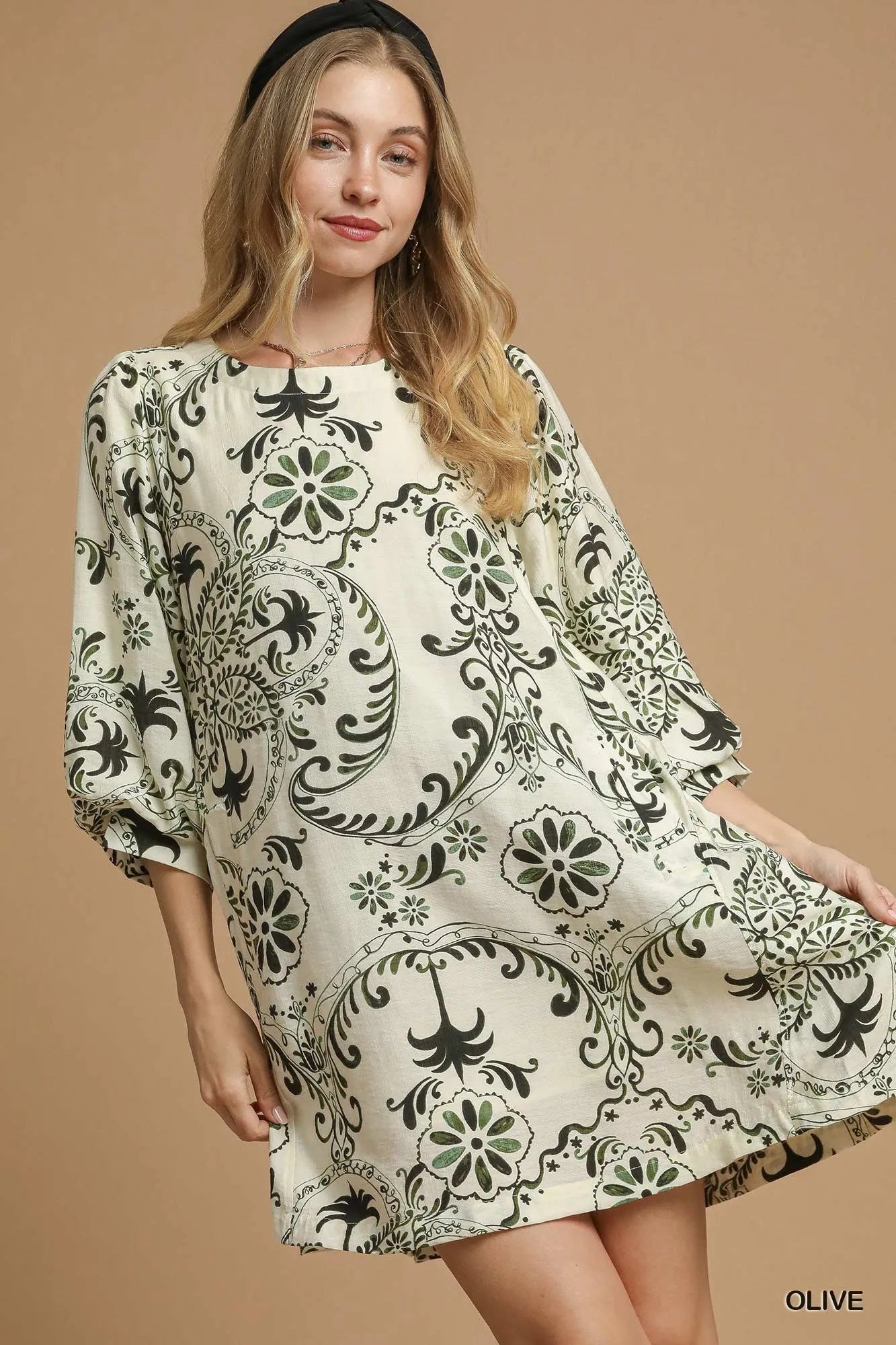 NEWYORKLISTED STYLE COLLECTION: Woman wearing a patterned dress on a beige background