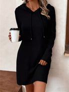 NEWYORKLISTED Comfort Collection: Person wearing a black hoodie dress holding a coffee cup indoors.