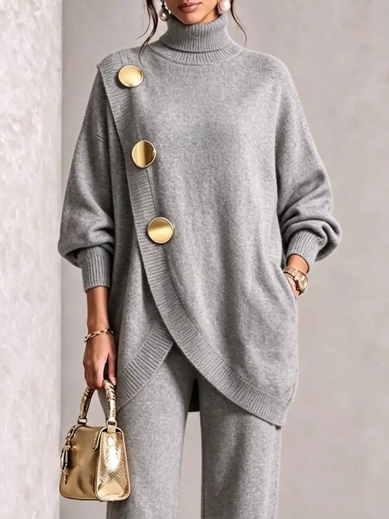NEWYORKLISTED STYLE COLLECTION:  A woman wearing a light gray knit turtleneck sweater with oversized gold buttons and matching gray knit pants, holding a small gold handbag against a neutral indoor background.