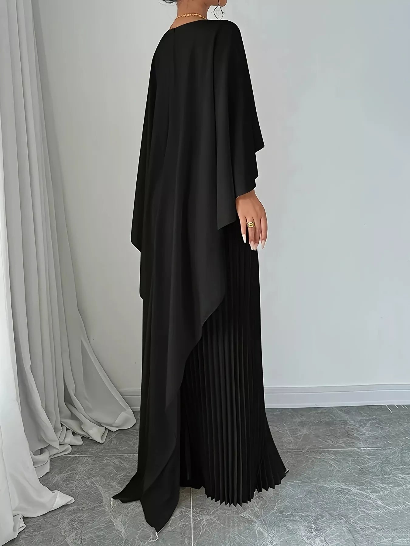 NEWYORKLISTED STYLE COLLECTION: Black pleated dress worn by a person against a white wall.