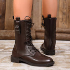 NEWYORKLISTED SHOE COLLECTION: A pair of dark brown leather lace-up combat boots worn on a mannequin or model's legs, shown against a rustic wooden background.