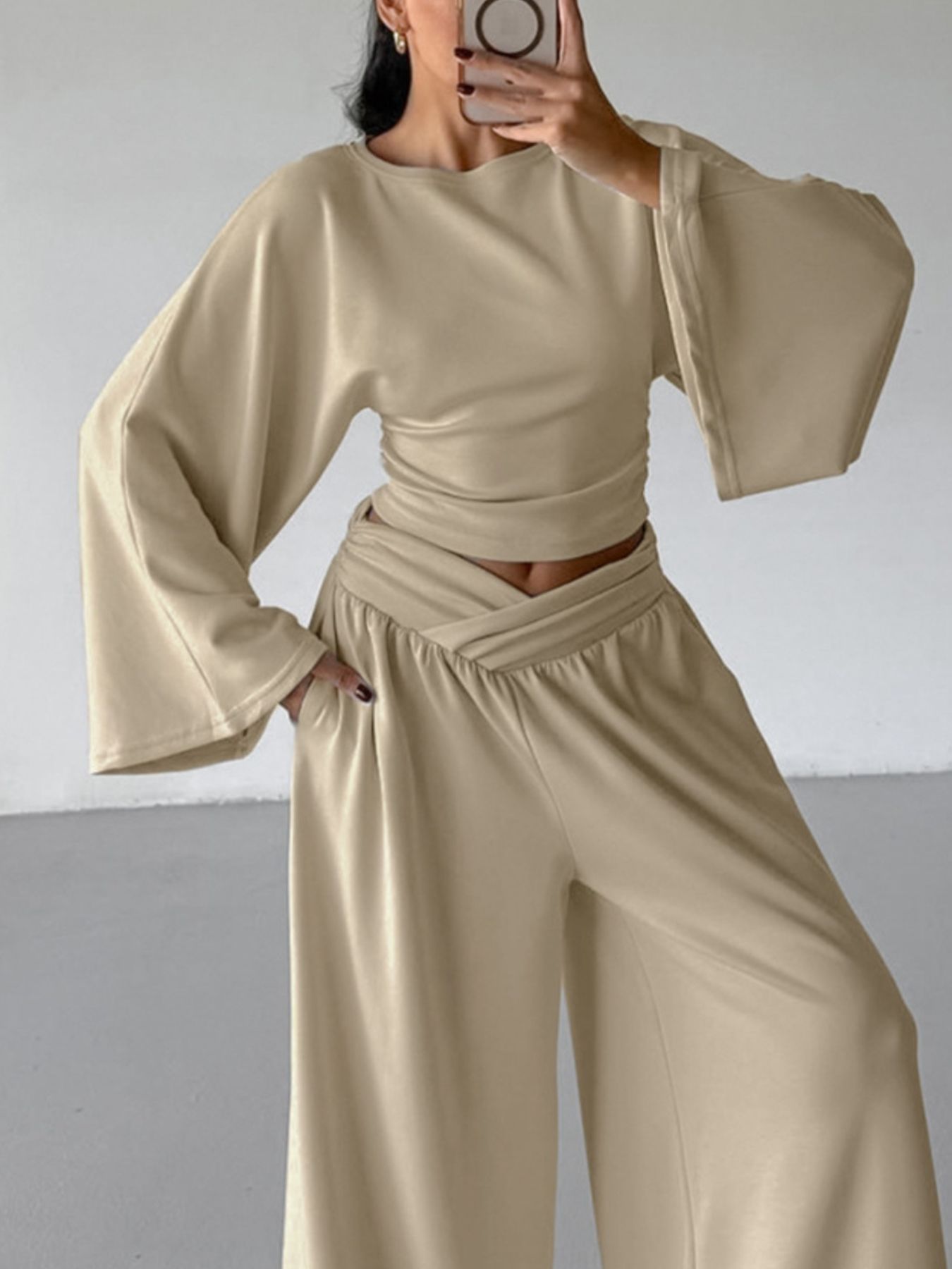 NEWYORKLISTED STYLE COLLECTION: Person wearing a beige outfit with wide sleeves and high-waisted pants against a plain background