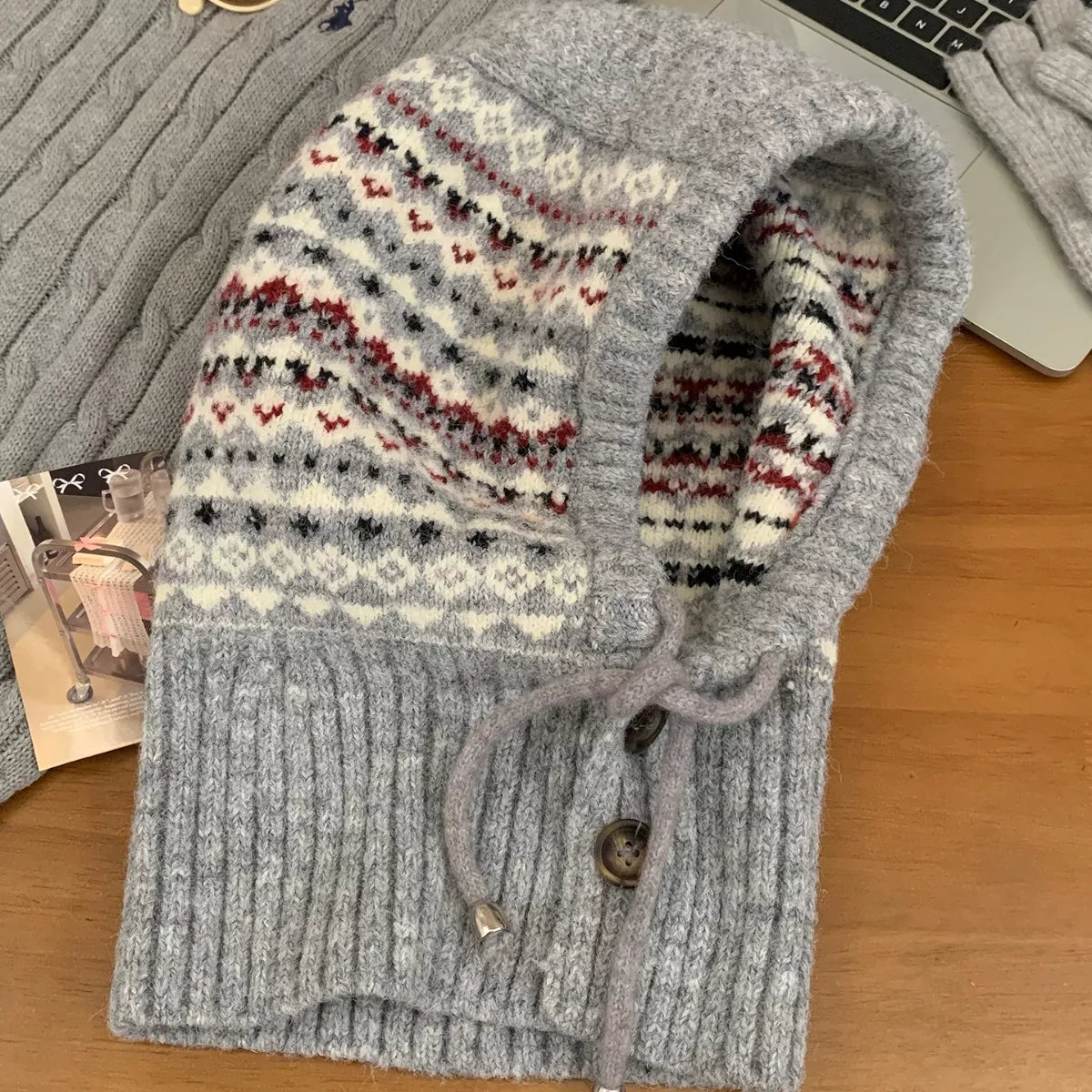 NEWYORKLISTED STYLE COLLECTION: Drawstring Knitted Winter Hat – Cozy, Chic & Cold-Weather Ready Gray knitted hoodie with patterned hood on a wooden surface