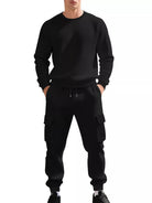 NEWYORKLISTED ATLAS MEN'S COLLECTION: A man wearing a black long-sleeve crewneck sweatshirt and matching black cargo jogger pants with a subtle geometric pattern, shown against a plain white background.