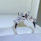 NYLD Glamour Collection By NEWYORKLISTED: Silver ring with a large central diamond and smaller side stones on a white background