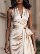 NEWYORKLISTED STYLE COLLECTION: Woman wearing a beige halter neck dress with a bow detail against a blurred background
