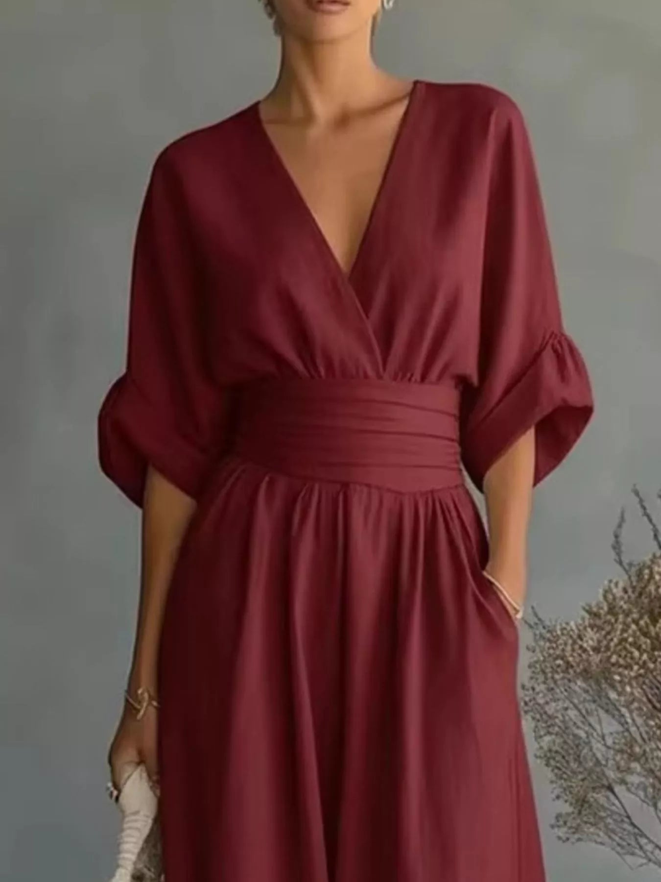 NEWYORKLISTED STYLE COLLECTION: A woman wearing a deep burgundy wrap-style dress with a V-neckline, gathered waist, and elbow-length puff sleeves, standing against a soft gray studio background.