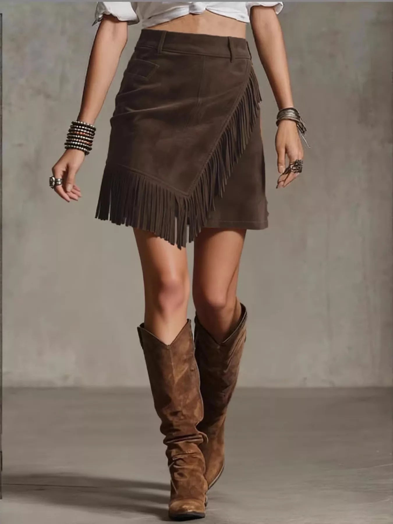 NEWYORKLISTED STYLE COLLECTION: Person wearing a brown suede skirt with fringe and matching knee-high boots on a neutral background