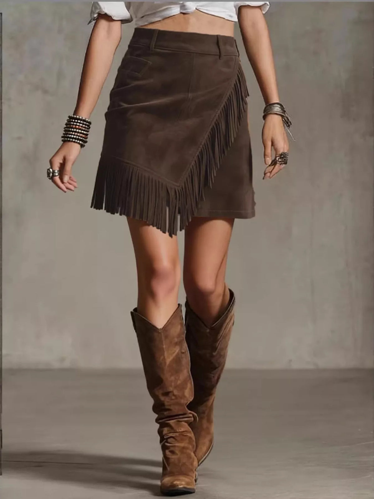 NEWYORKLISTED STYLE COLLECTION: Person wearing a brown suede skirt with fringe and matching knee-high boots on a neutral background
