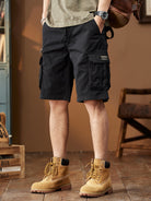 NEWYORKLISTED ATLAS MEN's COLLECTION: Person wearing black cargo shorts and tan boots in a room with wooden floor and furniture.