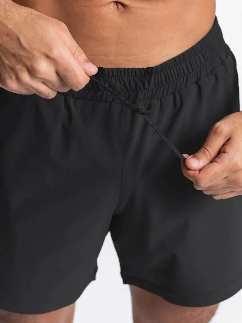 NEWYORKLISTED ATLAS MEN'S COLLECTION: Person adjusting the waistband of black shorts on a plain background