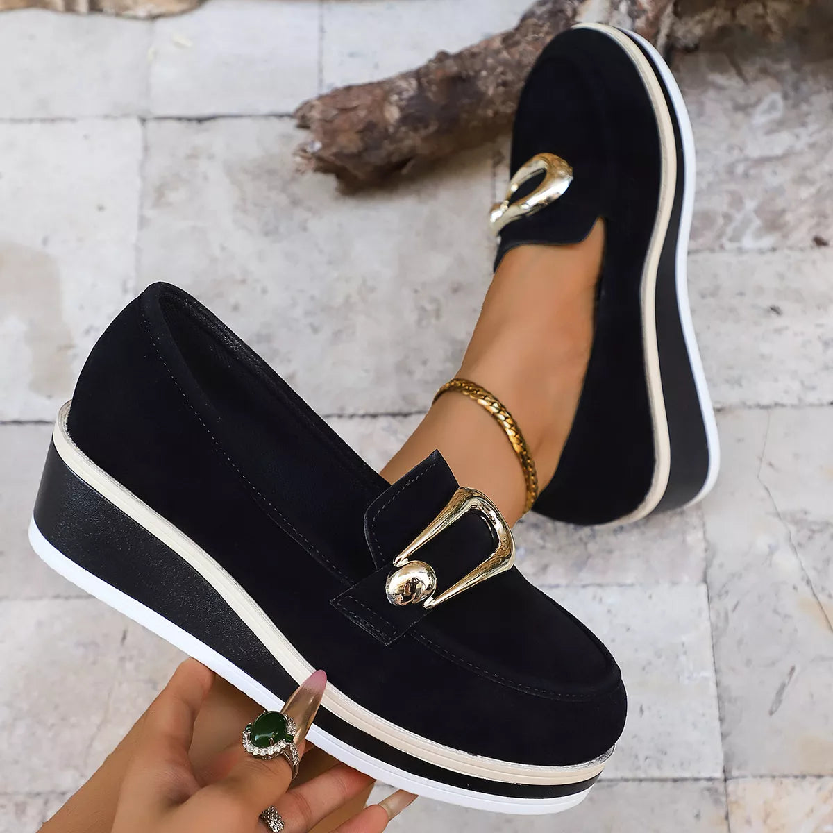 NEWYORKLISTED SHOE COLLECTION: Black loafers with gold buckles worn by a person on a light stone floor.