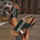NEWYORKLISTED SHOE COLLECTION: A pair of dark green leather slide sandals with burgundy straps and light beige lining, shown on a rustic wooden surface with one sandal worn and the other held in a hand.
