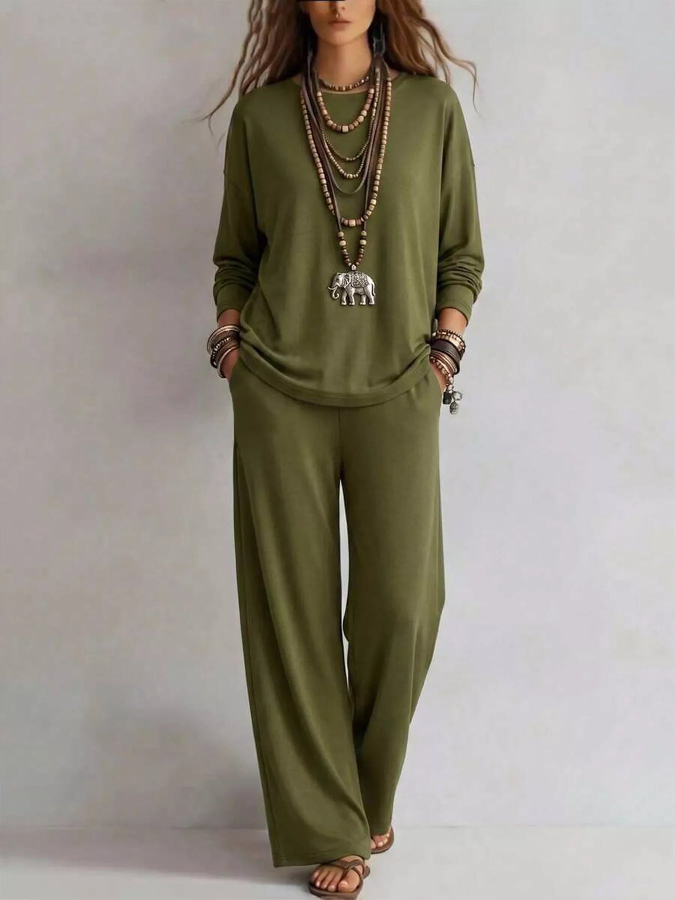 NEWYORKLISTED STYLE COLLECTION: A woman modeling a matching olive green lounge set consisting of a long-sleeve top and wide-leg pants, styled with layered necklaces and bracelets against a plain light gray background.