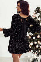 NEWYORKLISTED Valentine's Day Specials: Woman wearing a black sequin dress with a bow tie in front of a decorated Christmas tree.