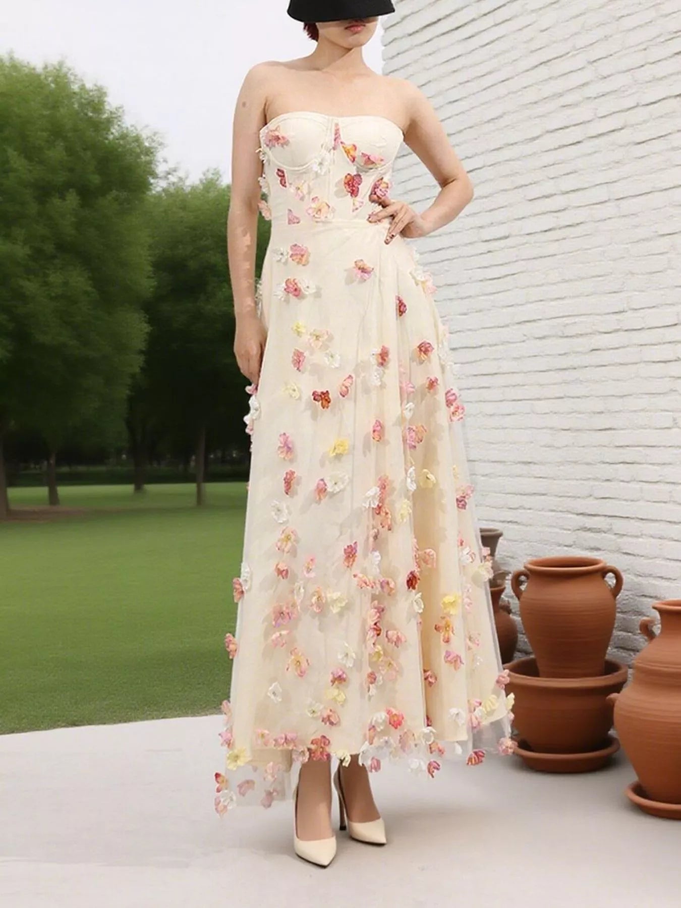 NEWYORKLISTED STYLE COLLECTION: Woman wearing a strapless floral dress standing in front of a white brick wall with greenery.