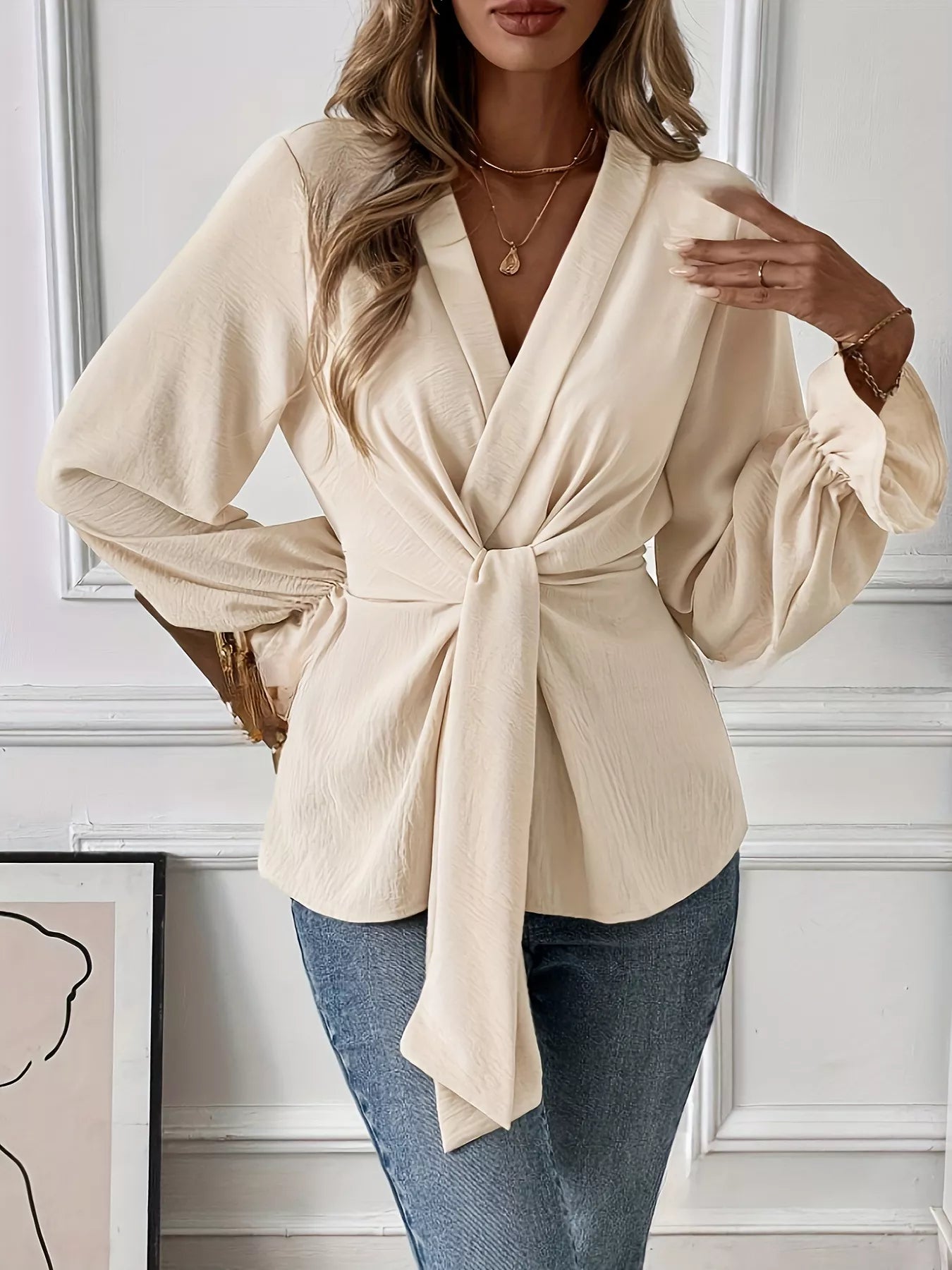 NEWYORKLISTED STYLE COLLECTION: Woman wearing a beige wrap blouse with long sleeves in an indoor setting.