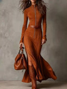 NEWYORKLISTED STYLE COLLECTION: Woman wearing a long brown dress with a belt, holding a matching handbag against a neutral background.