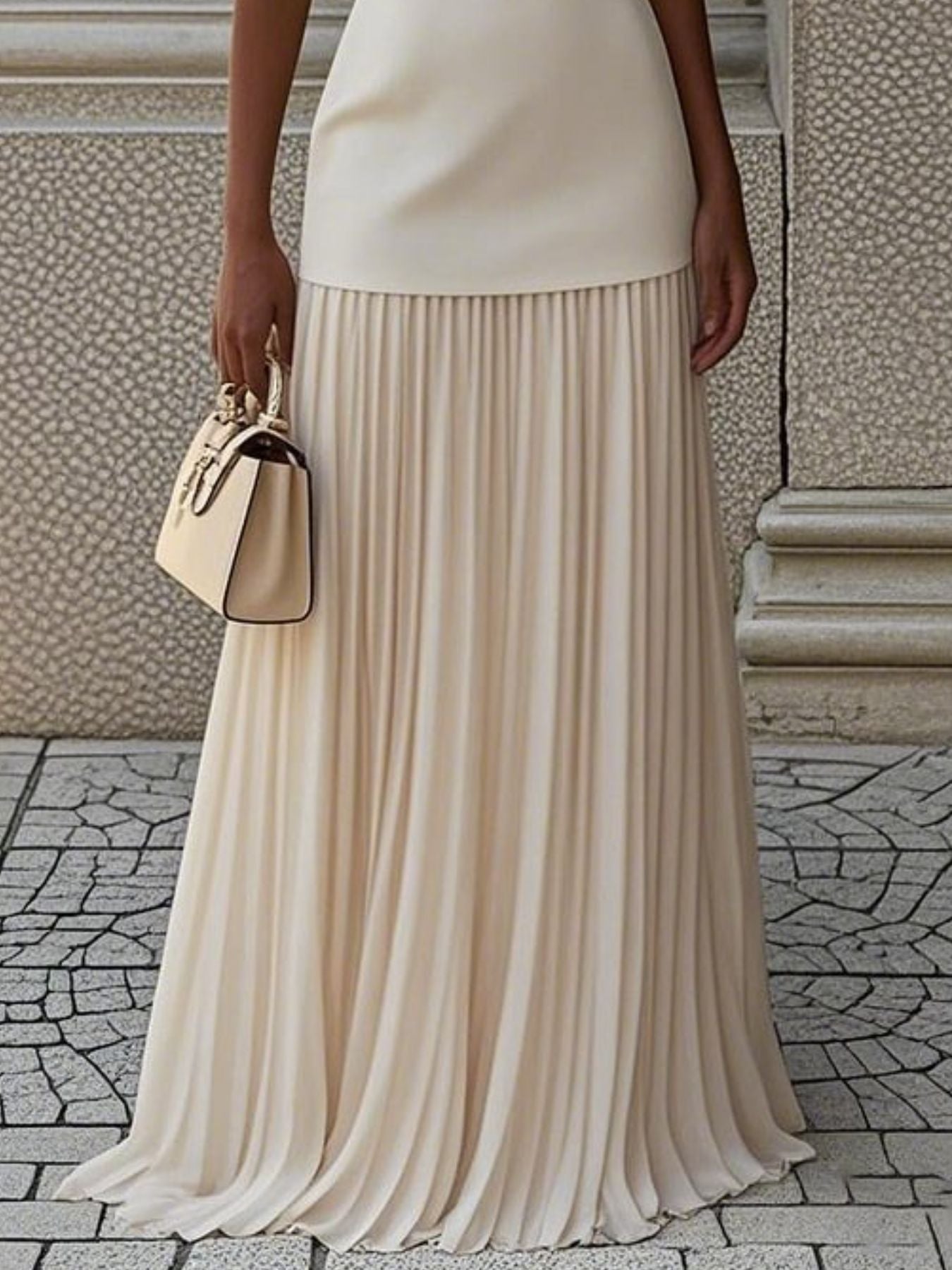 NEWYORKLISTED STYLE COLLECTION: Person wearing a beige pleated skirt holding a matching handbag on a stone pavement.