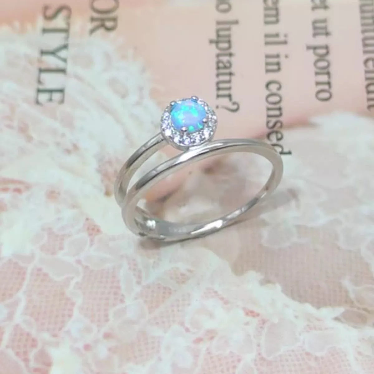 NYLD Glamour Collection by NEWYORKLISTED: Silver ring with a blue gemstone on a textured fabric background