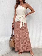 NEWYORKLISTED STYLE COLLECTION: Woman wearing a white one-shoulder top and patterned skirt against a light gray wall.