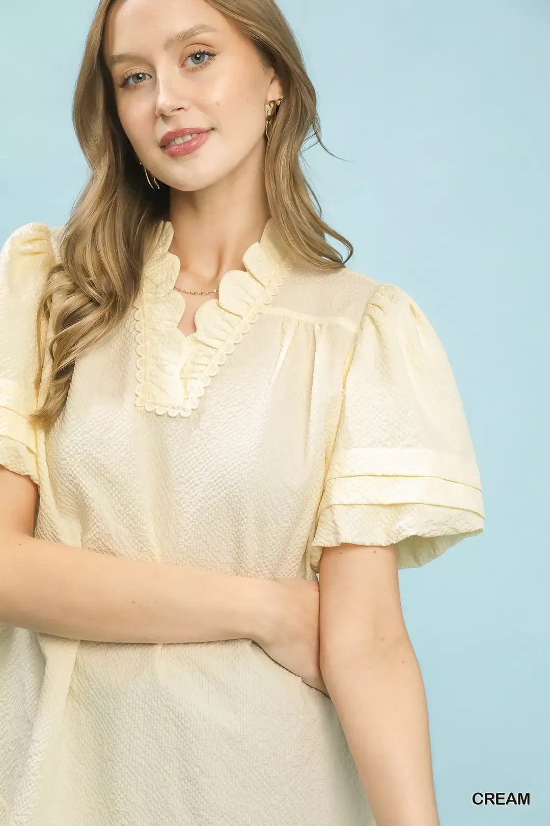 NEWYORKLISTED Style Collection: Woman wearing a cream-colored dress with ruffled sleeves against a light blue background