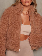 NEWYORKLISTED STYLE COLLECTION: Person wearing a brown sherpa jacket with a neutral background