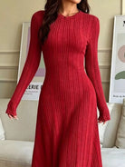 NEWYORKLISTED STYLE COLLECTION: A woman wearing a long-sleeve, ribbed knit midi dress in a deep red color, standing in a living room setting.