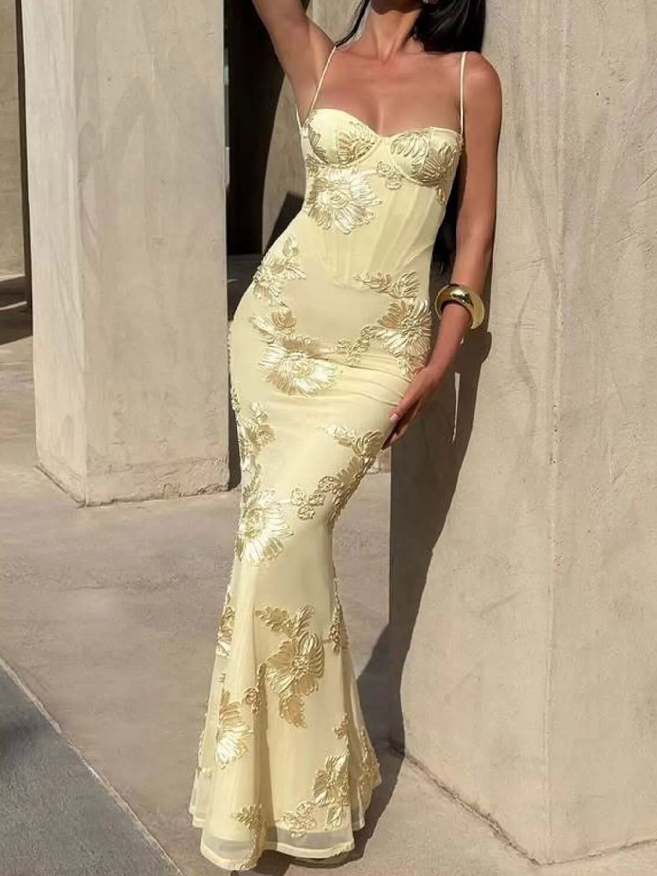 NEWYORKLISTED STYLE COLLECTION: Woman wearing a yellow evening gown with floral embroidery against a stone wall.
