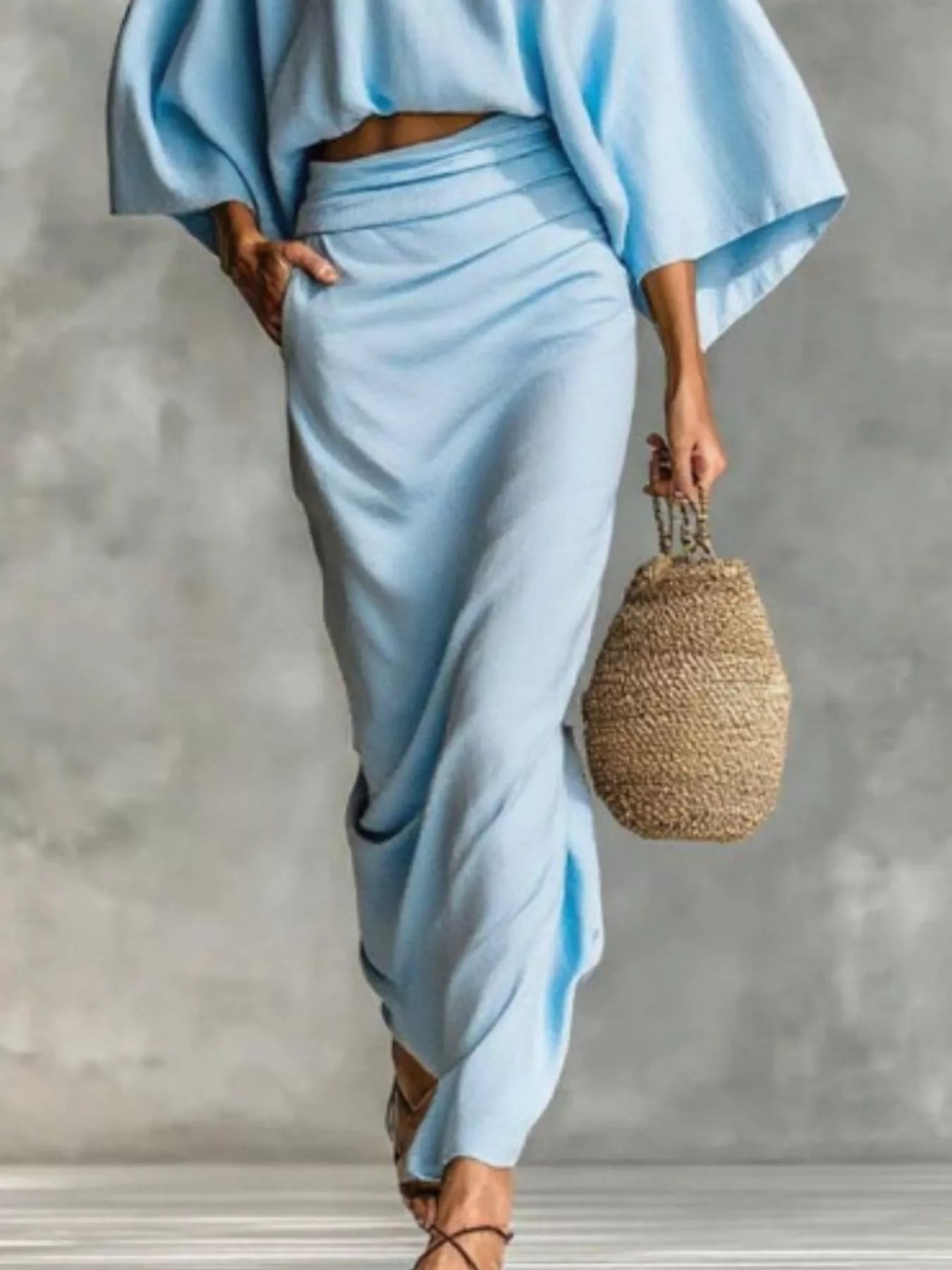 NEWYORKLISTED STYLE COLLECTION: Person wearing a light blue outfit holding a woven bag against a gray background