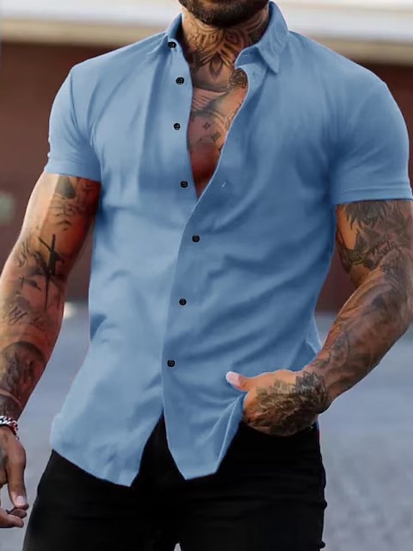 NEWYORKLISTED ATLAS MEN's COLLECTION: Man wearing a light blue button-up shirt with tattoos on arms, standing against a blurred background.